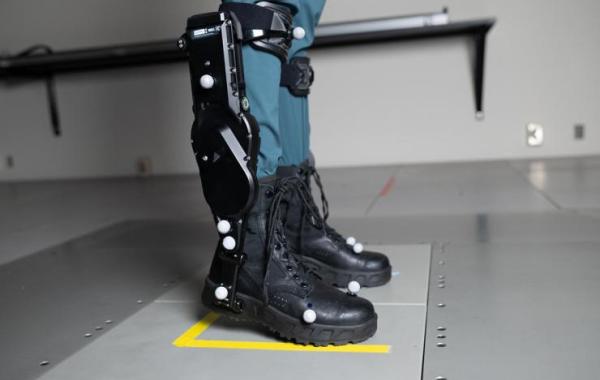 A person wearing black robotic exoskeleton boots standing on a gray platform.