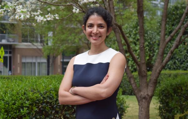 Farzaneh Najafi standing outside smiling with her arms crossed. Green foliage is visible in the background.