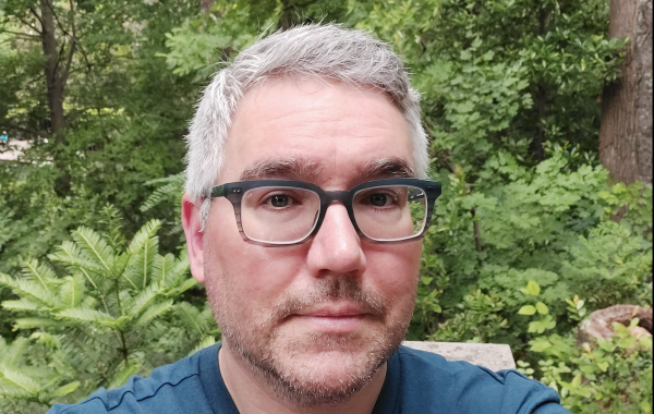 A man with glasses in front of greenery