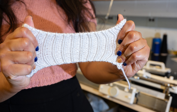 Hands stretching a small piece of white knit fabric to show its elasticity