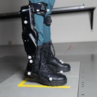 A person wearing black robotic exoskeleton boots standing on a gray platform.