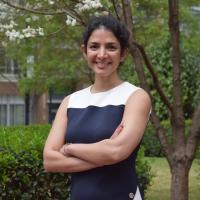 Farzaneh Najafi standing outside smiling with her arms crossed. Green foliage is visible in the background.